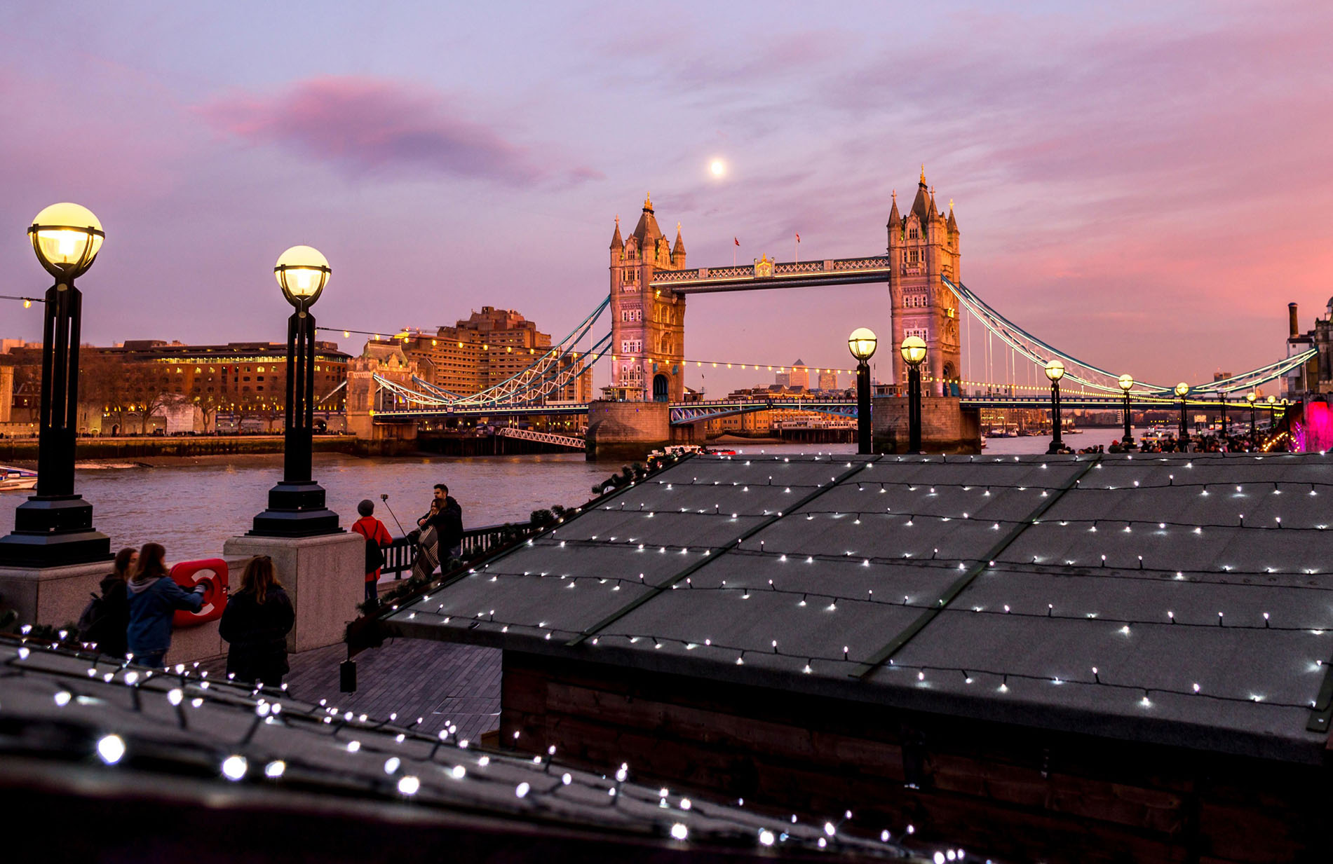 London Tower Bridge at a beautiful full moon evening with Christmas market huts with lights in the foreground.