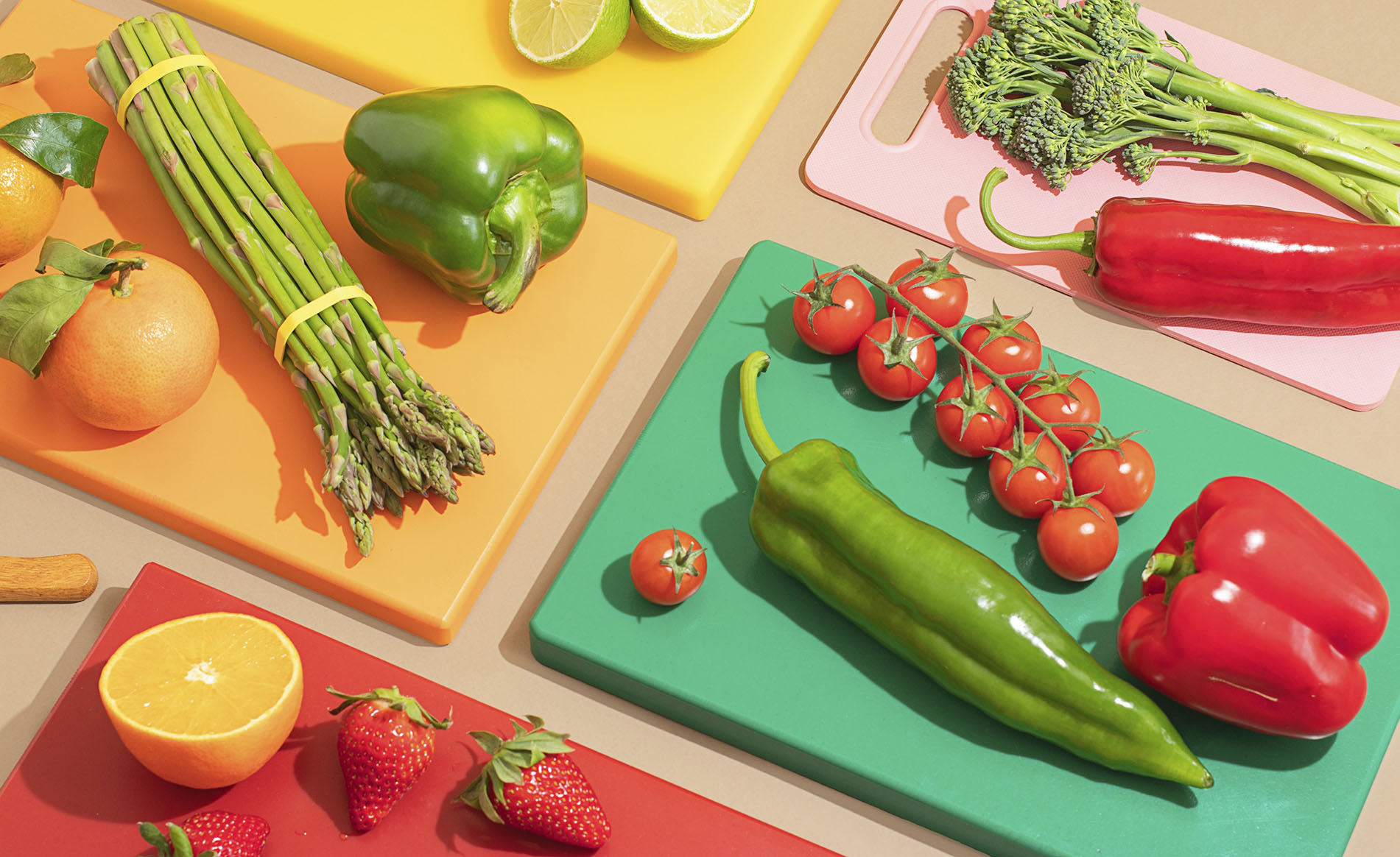 A colorful and artistic display of fresh vegetables and fruits on vibrant cutting boards. Includes peppers, lime, tomatoes, asparagus, strawberries, and oranges