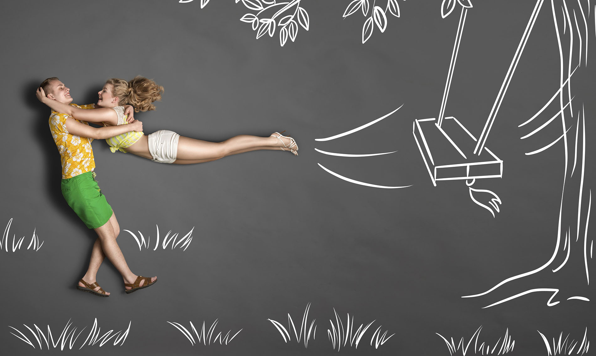 Happy Valentine's Day love story concept of a romantic couple against chalk drawings background. Male catches his girlfriend jumping from tree swinging