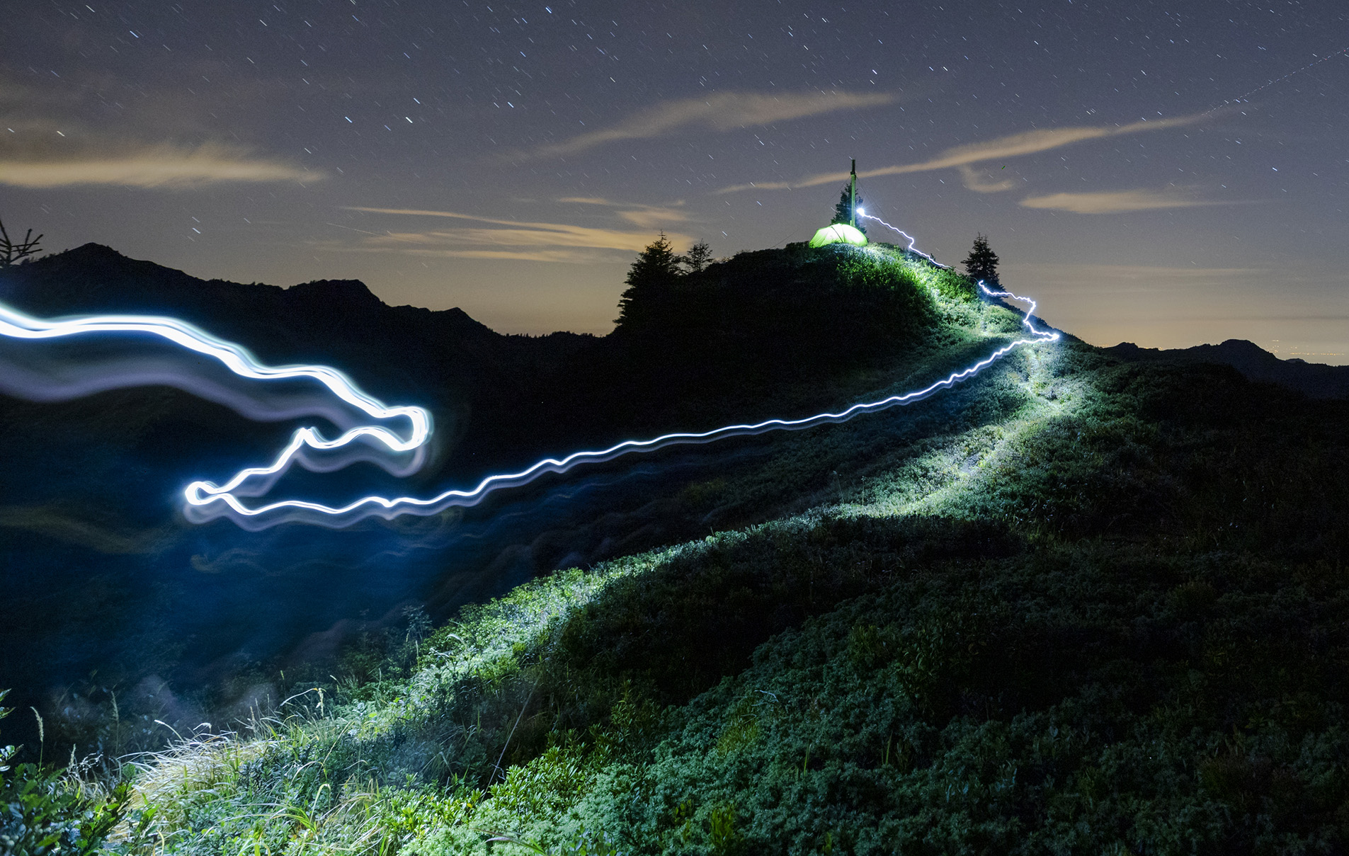 Green tent and tracer with headlamp under a starry sky on the Portlakopf