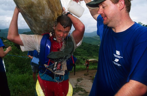 guy pours jug of water over another carrying a canoe