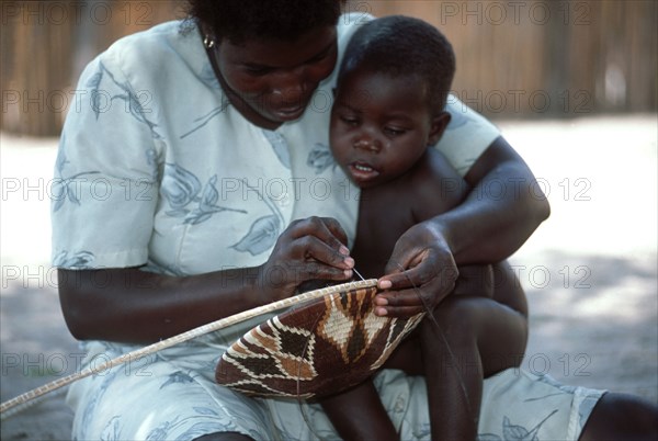 Lady weaving a basket with watching child