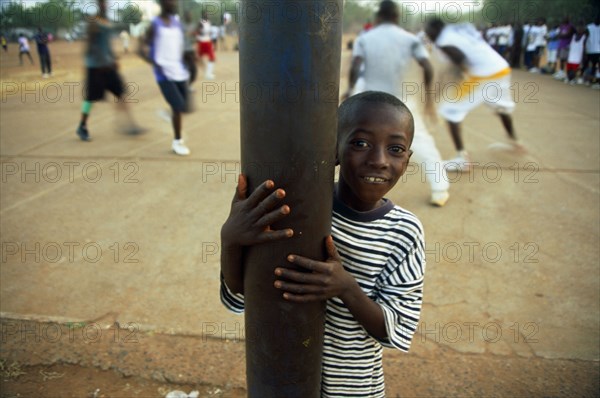 In the suburb of Corofina Nord, Bamako, Mali, young people gather in the late afternoon at a large dusty field to play sport - basketball and soccer - socialise, and play. The field seems to be the centre of social life in the area. 

Young boys spectate a game of basketball