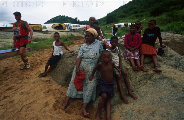 Family sitting on rock, canoeists running behind