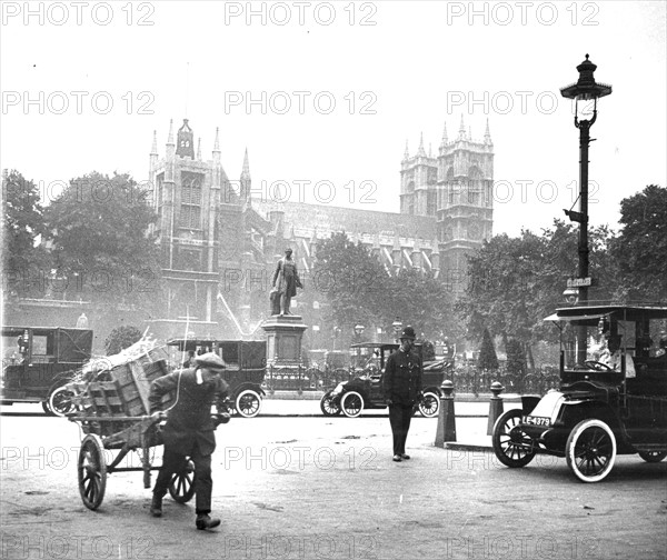 Street scene, Westminster, London, with cars, boy with handcart, and policeman on duty, c 1910.  Photograph.