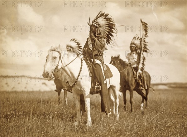 Three Native American chiefs mounted on horses and wearing feather headdresses