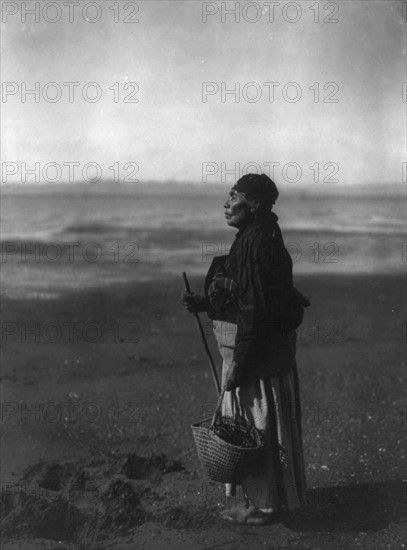 American Indian woman standing holding basket on beach