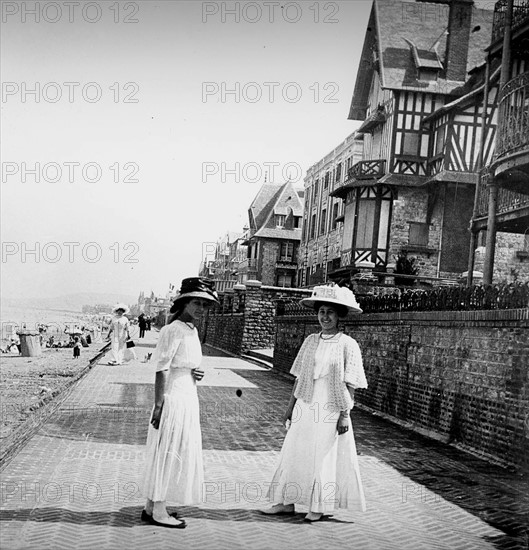 Two young women walk along a promenade by a beach in France, during summer