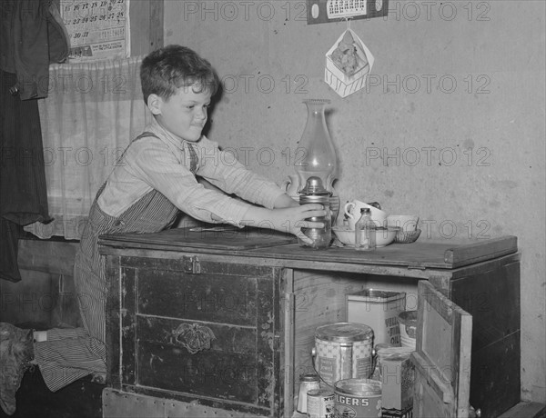 Son of migrant worker reaching for lamp atop cabinet in trailer home. Weslaco, Texas. 19390101