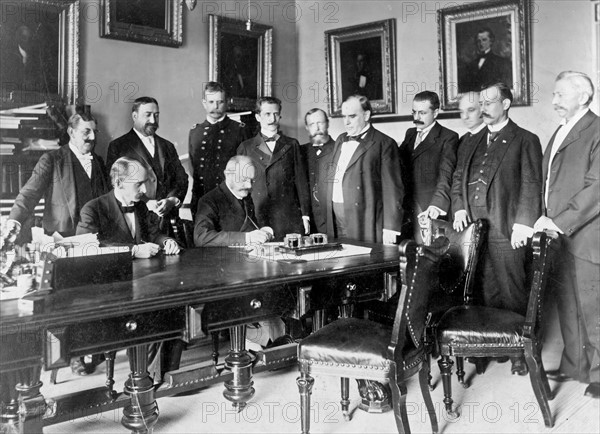 Photograph of French Ambassador Pierre Paul Cambon signing the Peace Protocol, as President William McKinley and others watch