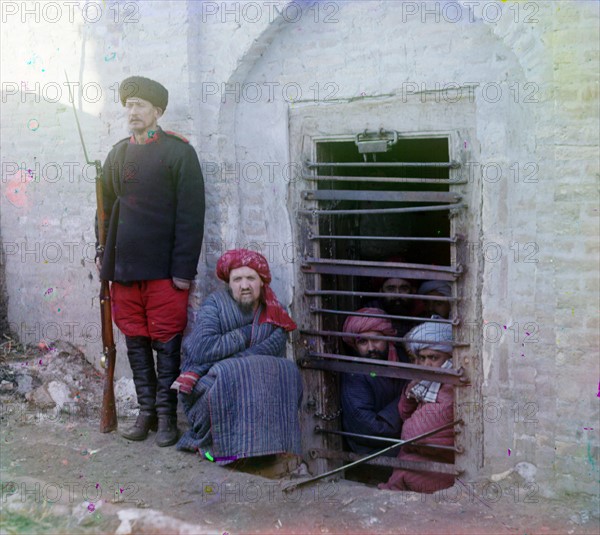 Zindan (prison), with inma: with inmates looking through the bars and a guard with Russian rifle, uniform and boots.