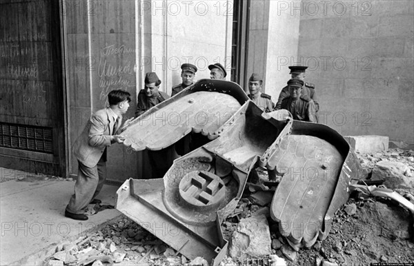 Photograph of Russian soldiers and a civilian struggle to move a large bronze Nazi Party eagle