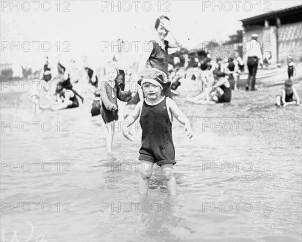 Young child at the edge of a beach crying as his family look on