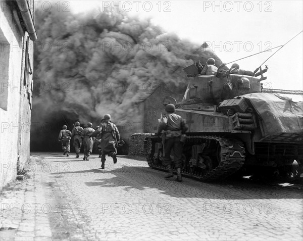 Photograph of M4 Sherman tank move through a smoke filled street in Wernberg