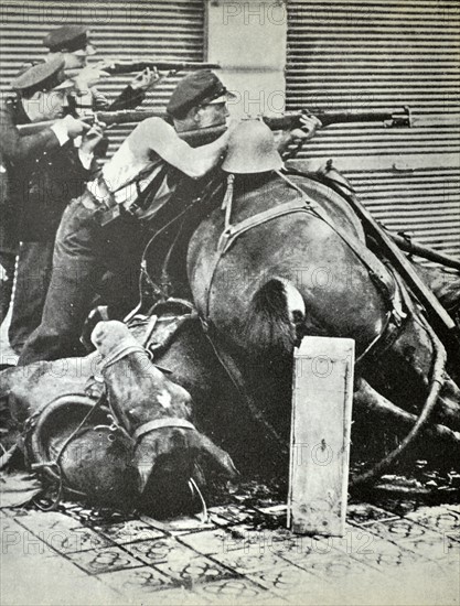 Three republican fighters take aim with rifles, behind a barricade made up of dead horses