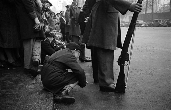 Child peers through legs to catch Princess Elizabeth's wedding.