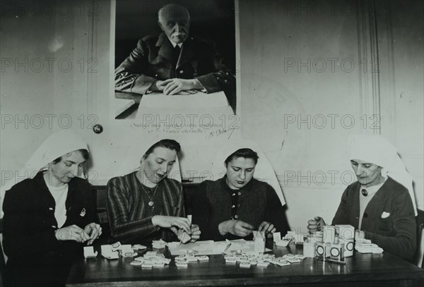 Photograph of a group of Vichy French nurses packs medical supplies under a portrait Of General Phillipe Petain, during the German occupation of France 1941