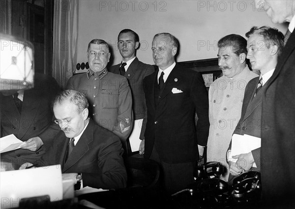 "Grenzvertrag D/UdSSR - W. Molotow unterzeichnet den Vertrag, im Hintergrund: J. v. Ribbentrop (3.v.r.); J. Stalin (2.v.l.)"