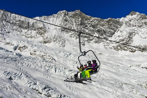 Skiers on a chairlift in front of the Feegletscher and the peaks Dom and Lenzspitze