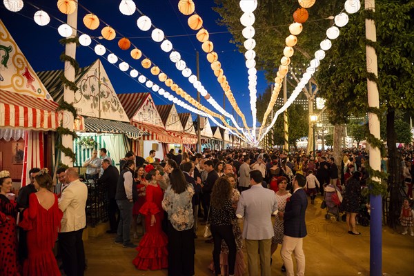 Spaniards celebrating in traditional clothes in front of lit marquees