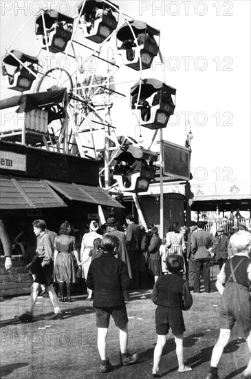 People walk over the fairground and look at the ferris wheel