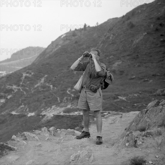 Man standing on a mountain path looking through binoculars