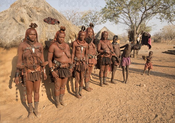 Himba women with children in front of a sleeping hut