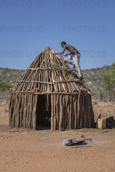 Man of the people of Ovahimba or Himba builds on the roof of a wooden hut