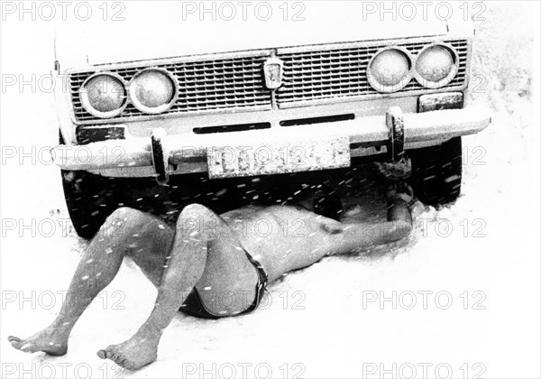 Man lies naked under a car in the snow ca. 1970s