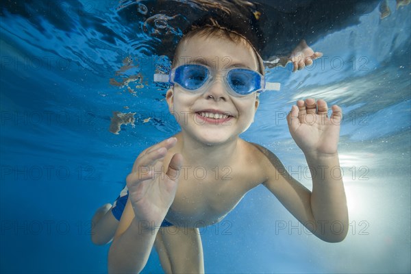 Young boy wearing swimming goggles dives in a pool