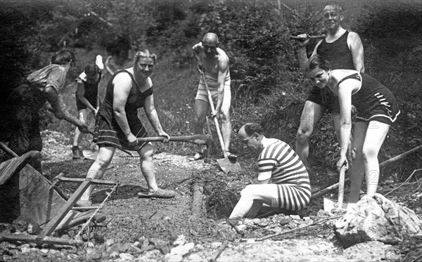 Men and women dig a hole wearing swimwear