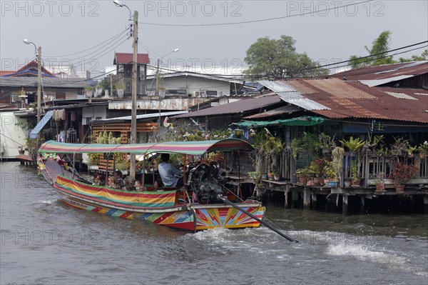 Canal with longtail boat and wooden houses on stilts