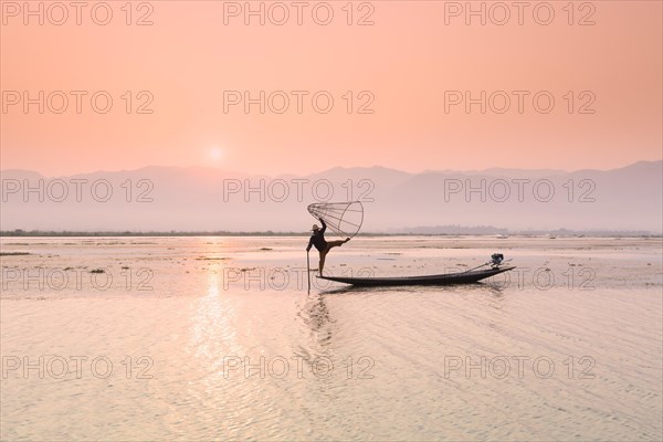 Inle lake fisherman standing on a longtail boat in the distinctive leg rowing stance used by the Intha people
