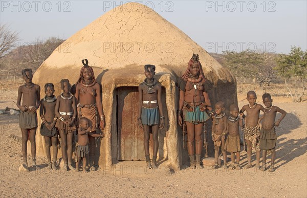 Himba women with children in front of a sleeping hut