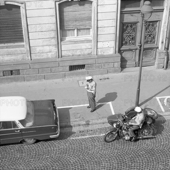 Two traffic policemen handing out a parking ticket to a car parker around 1950