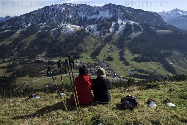 Two hikers sit in the grass and enjoy the view of Oberjoch and the Iseler