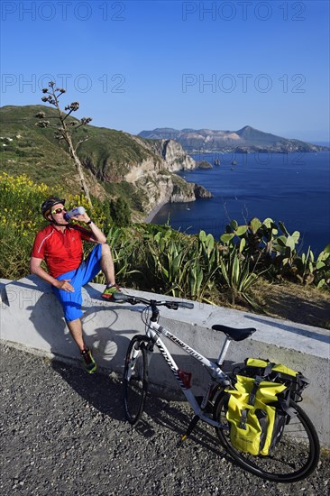 Cyclist pausing on the Belvedere Quattrocchi with a view over the rocks Faraglione on the island Vulcano