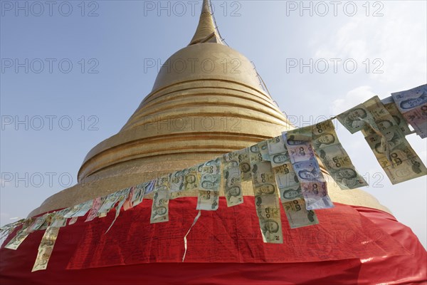 Thai banknotes are hanging on a leash in front of the golden Chedi
