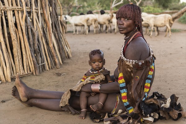 Woman with toddler sitting in front of mud hut on the ground