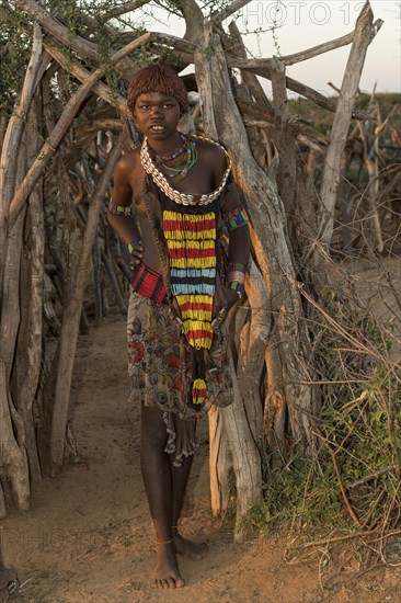 Girl approx. 15 years of the Hamer tribe in traditional clothes in front of hut