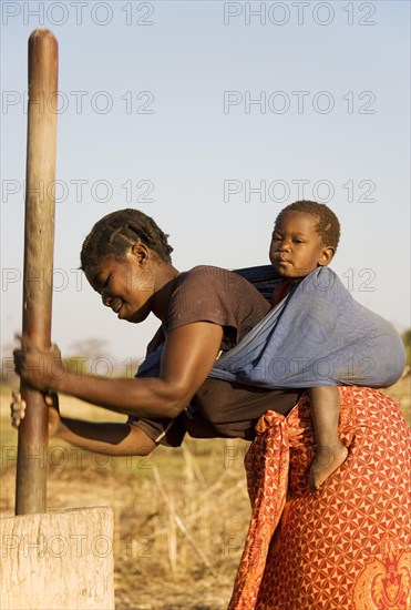 Tonga woman with child on her back pounding grain