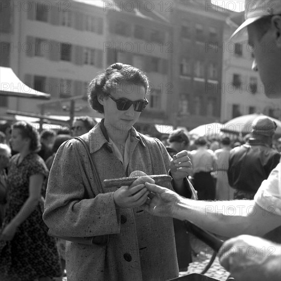 Seller hands a woman a sausage in bread