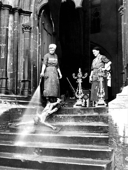 Two cleaning ladies spray crucifix with Jesus