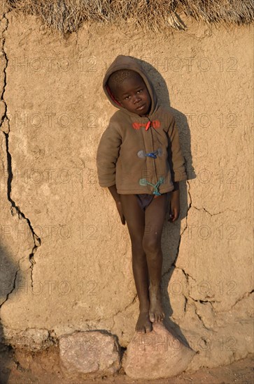 Himbajunge leans on mud hut