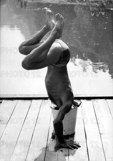 Man makes handstand and sticks head in bucket ca. 1970s