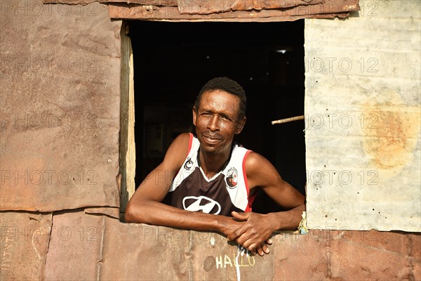 Local man looking out of the window of his poor corrugated iron hut