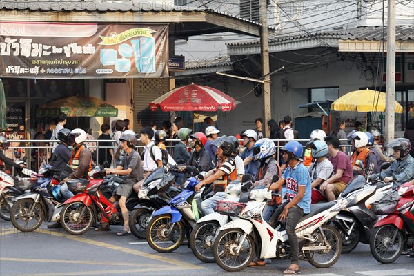 Many moped drivers are waiting at an intersection