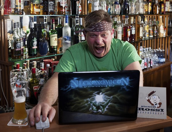 Man in internet cafe looks on the laptop and shouts in shock