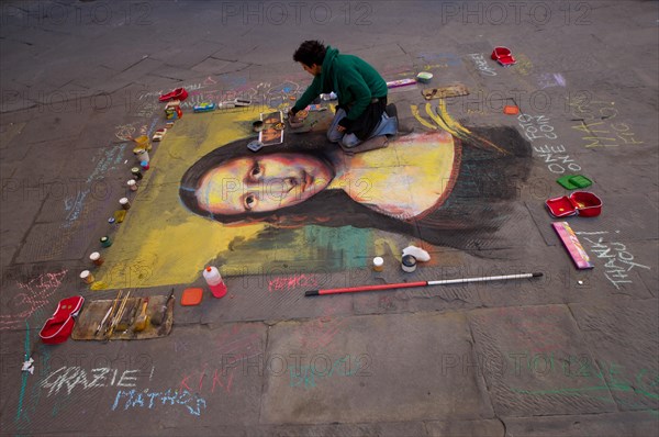Street artist paints the Mona Lisa by Leonardo da Vinci with chalk on the asphalt