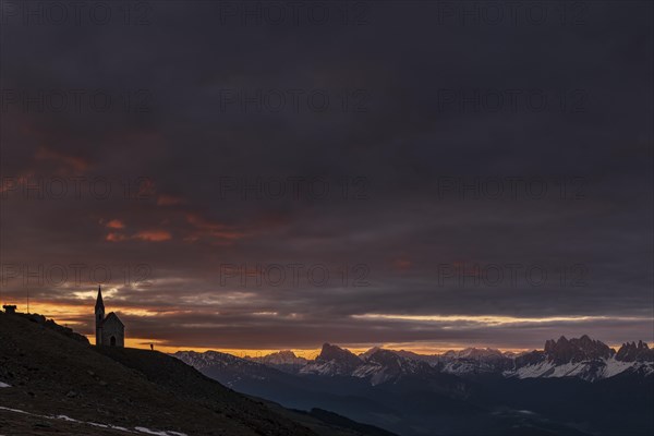 Latzfonser cross chapel at sunrise with dramatic clouds and South Tyrolean mountains